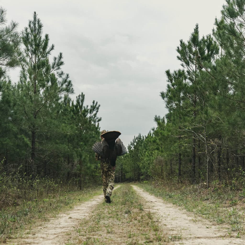 Man dressed in camo carrying a turkey down a path