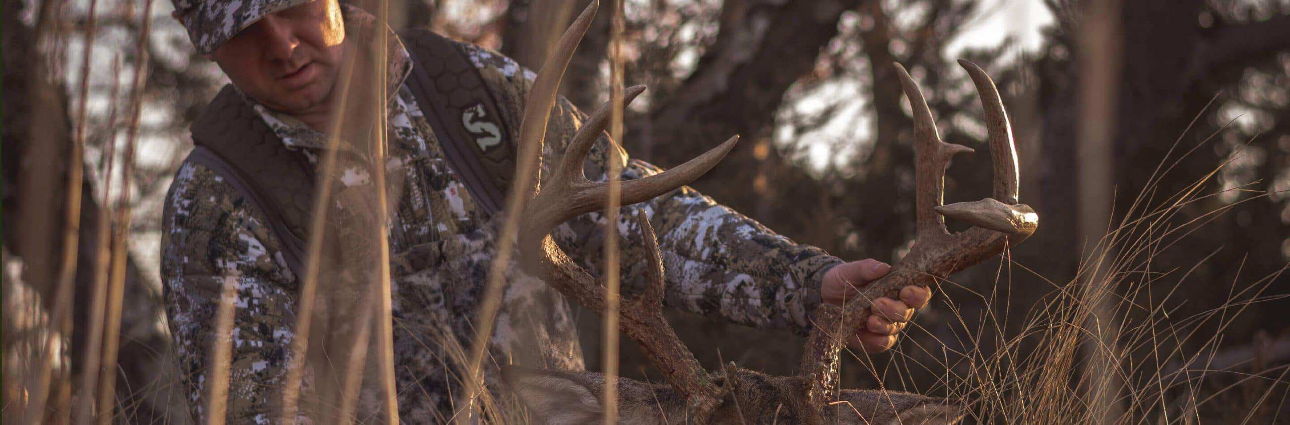 Man dressed in camo holding deer antlers