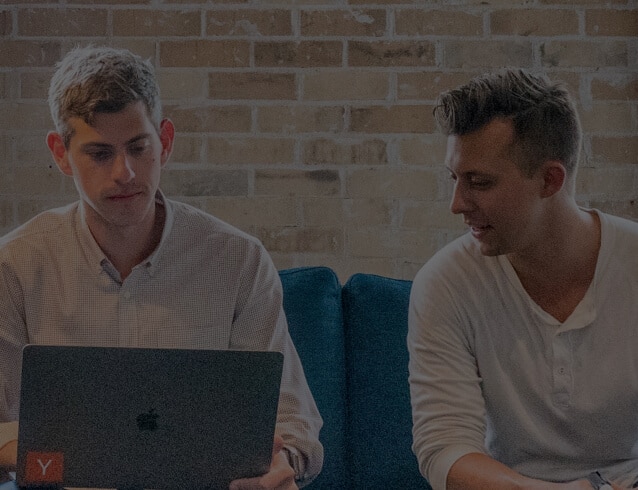 Two young men sitting on a blue couch working on a laptop