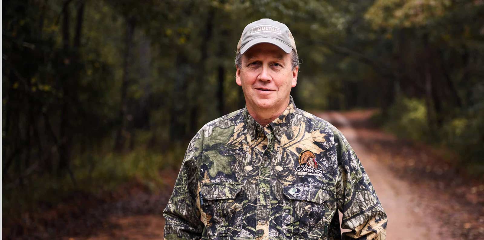 Man dressed in camo standing on a trail in the woods